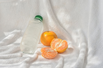 Fresh orange fruits and cold water bottle as refreshments after workout class, white towel background.