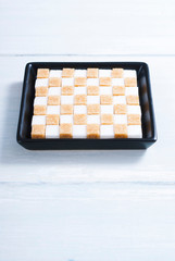 white and brown sugar nubs on black square plate, bright wood table background