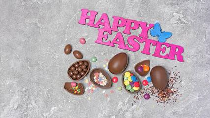 Pink text of happy easter and chocolate traditional eggs with bright colorful sugar sprinkles