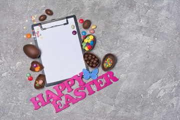 Mock up of clipboard with pink text of happy easter and chocolate traditional eggs.