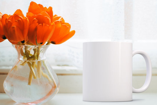 White Mug Mockup - Easter theme. Blank mug next to a bunch of orange tulips in a glass vase on a window ledge. Perfect for businesses selling mugs, just overlay your quote or design on to the image.	