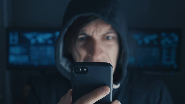 Angry Hacker in hood using smartphone. Cybercriminal screams and show aggression