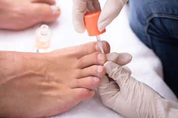 Manicurist Applying Moisturizing Nail Oil To Man's Feet