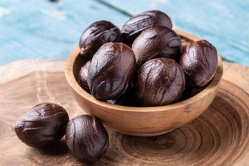 Whole inshell nutmeg nuts in a bowl on blue rustic wooden table.