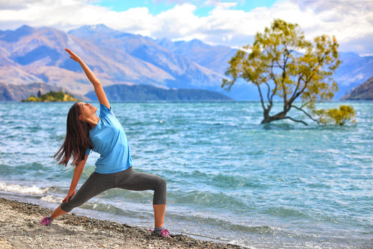 Yoga travel New Zealand. Asian girl practicing yoga at the lone tree in Wanaka lake, NZ. Woman training fitness for a healthy body and mind, meditating in the summer outdoor.