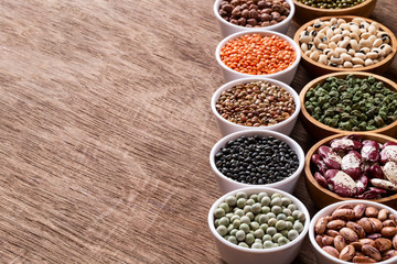 Various assortment set of indian legumes in bowls on wooden background with copyspace.