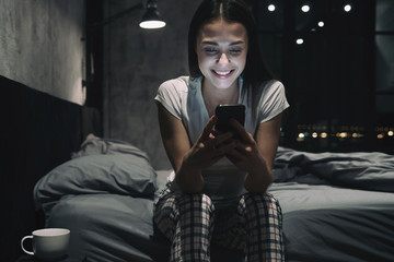 Portrait of young smiling woman chatting with smartphone at night