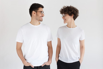 Young smiling couple in blank white t-shirts looking at each other, isolated on gray background
