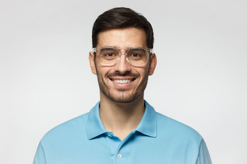 Smiling modern nice guy in blue polo shirt and trendy trasparent eyeglasses, isolated on gray...