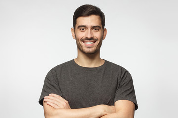 Portrait of smiling handsome man in grey t-shirt standing with crossed arms. isolated on gray...