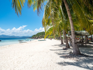 Perfect white sand beach in Philippines. Coconut Palm trees against blue sky, boat in ocean. Sunny...