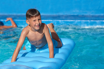 Caucasian boy having fun in swimming pool at resort. He is using inflatable mattress, enjoying his holidays and smilint to the camera.