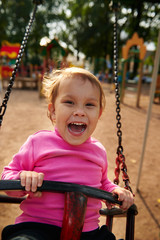 Little girl with funny facial expression swinging on the swings on the Playground