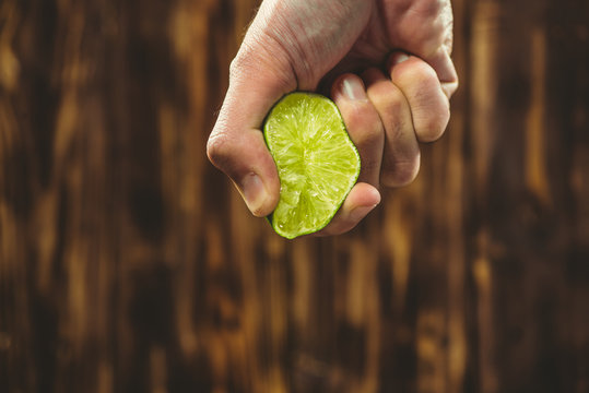 Hand Squeeze Lime With Lime Drop On Wooden Background