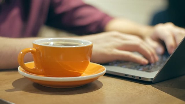 Close-up of male hands typing on a laptop and drinking coffee
