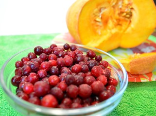 Fresh-frozen cranberries in a vase against a background of sliced pumpkin