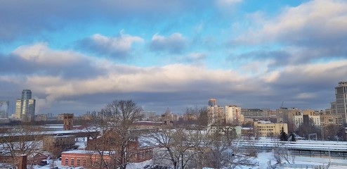 Dawn in Moscow over houses and a beautiful city sunrise reflected in the windows of high-rises and skyscrapers on a frosty winter morning with bright sky, clouds and smoke from the pipes of factories