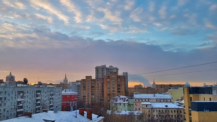 Fototapeta premium Świt w Moskwie nad domami i piękny wschód słońca miasta odbijający się w oknach wieżowców i wieżowców w mroźny zimowy poranek z jasnym niebem, chmurami i dymem z rur fabryk