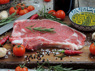 Raw meat steak, pepper, herbs, garlic and knife on wooden chopping board