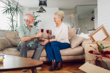 Cheerful senior couple moving into new home smiling at each other and drink wine.