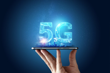Creative background, male hand holding a phone with a 5G hologram on the background of the city....