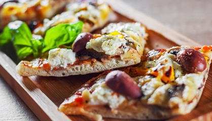 sliced vegetarian pizza with Mozzarella cheese, olives, mushrooms, pepper and fresh basil. Italian pizza on wooden table background