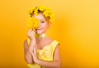 Portrait of a cute girl with freckles and a yellow wreath on her head. A girl in a yellow dress holding a yellow flower