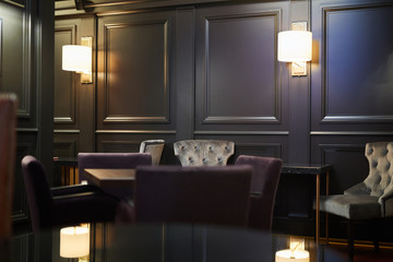 Lampen langs zwarte houten wanden, tafels en fauteuils voor gasten van luxe restaurant