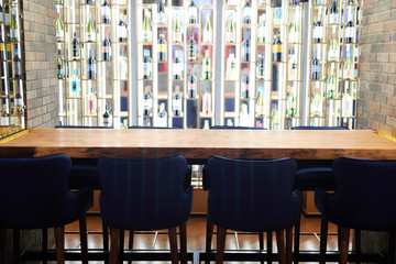 Eight blue armchairs around long table in front of bar wall with many bottles of alcoholic drinks