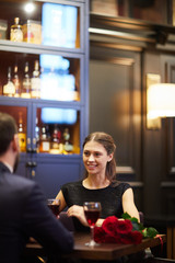 Pretty girl looking at her boyfriend while both sitting by table opposite one another and talking during date in restaurant