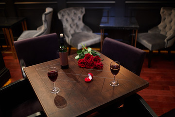 Wooden table with bottle of wine, two wineglasses, bunch of red roses and velvet box with...