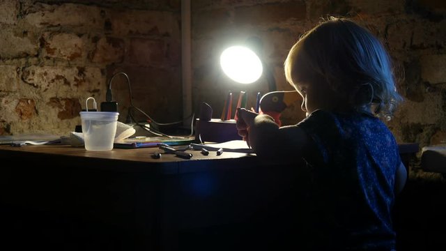 Kid is drawing in the album. Little girl, child sits near the window and painting