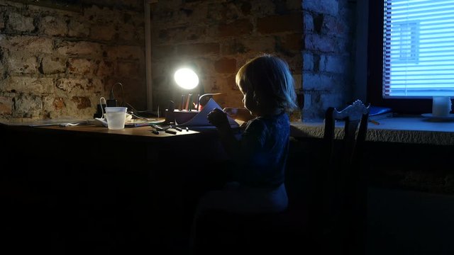 Kid is drawing in the album. Little girl, child sits near the window and painting