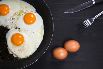 Fried eggs in a frying pan on a black surface
