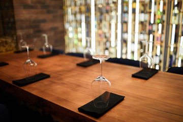 Wooden table in restaurant served with several wineglasses standing upside down on folded black...