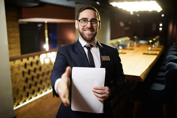 Cheerful director of restaurant in formalwear giving hand for handshake to one of guests