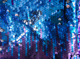 Bright shiny texture of colorful sequins in blue and purple colors. Fashion fabric background.