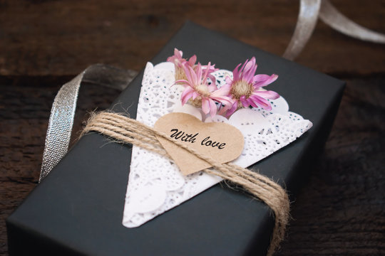 Valentines day craft gift box ideas. Black paper present box text WITH LOVE on heart, lace napkin, jute rope and silver on dark wooden background. Love, romance, handmade concept