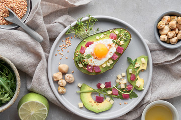 Keto diet dish: baked Avocado boat with ham cubes, quail egg and cheese served with green rucola...