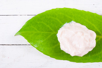 cosmetic cream on herbal leaf, white wood background