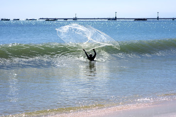 A fisherman in water throws his dragnet to the ocean 