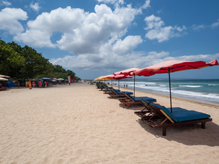 Colorful umbrellas stay on yellow sand beach with blue sea and blue sky on background. Concept for rest, relaxation, holidays, spa, resort. Kuta beach, Bali, Indonesia, October, 2018