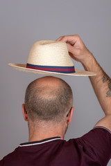 Balding man putting on a straw hat for sun protection.