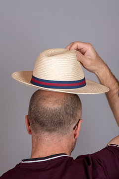 Balding Man Putting On A Straw Hat For Sun Protection.