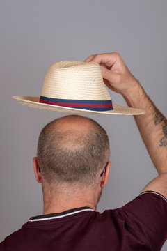 Balding Man Putting On A Straw Hat For Sun Protection.