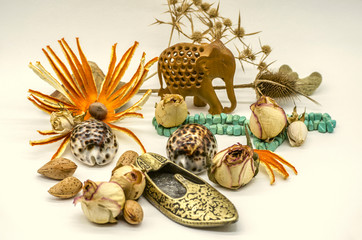 Group of old oriental souvenirs, wooden elephant figurine, turquoise beads, brass slipper in the form of ashtrays, dry buds, spikes, shells on a white background
