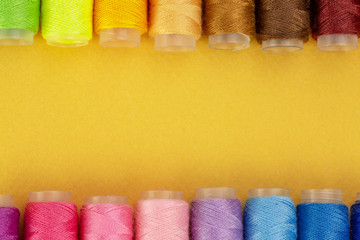 Colorful thread spools over bright yellow background, above view