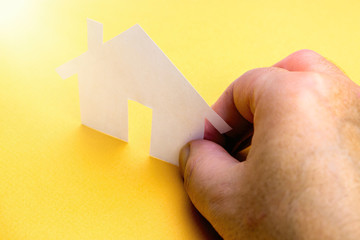 Hand holding a paper house on a yellow background.