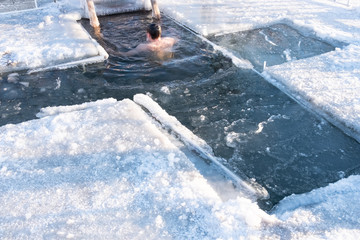 Holidays of Orthodox baptism. A man is immersed in ice water. Ice hole on the river in the ice in the form of a cross.