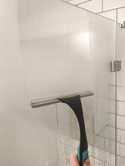 Cleaning concept - hand cleaning glass window pane in bathroom with shower wiper. Shower squeegee.